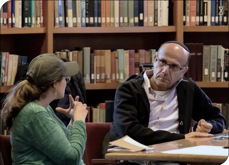 Alex Pomson talks to Nettie Aharon in front of library shelves with books